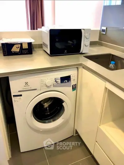 Modern kitchen with washing machine and microwave in compact layout.
