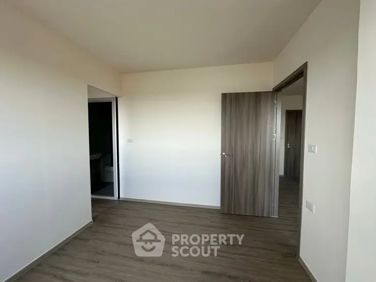 Spacious empty room with wooden flooring and modern door in a minimalist apartment.