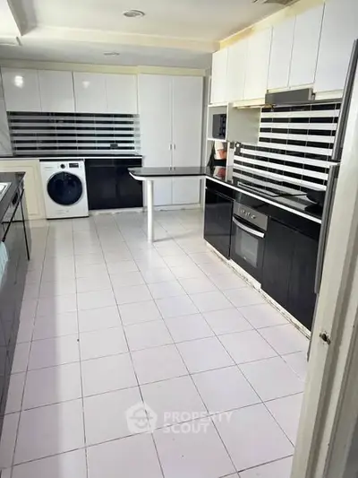 Modern kitchen with sleek black and white cabinetry, featuring built-in oven and washing machine.