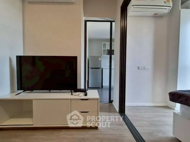 Modern living room with sleek TV unit and view into contemporary kitchen area.