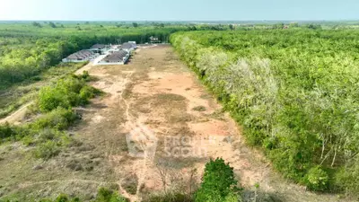 Expansive land plot with lush greenery and nearby residential development, ideal for investment.