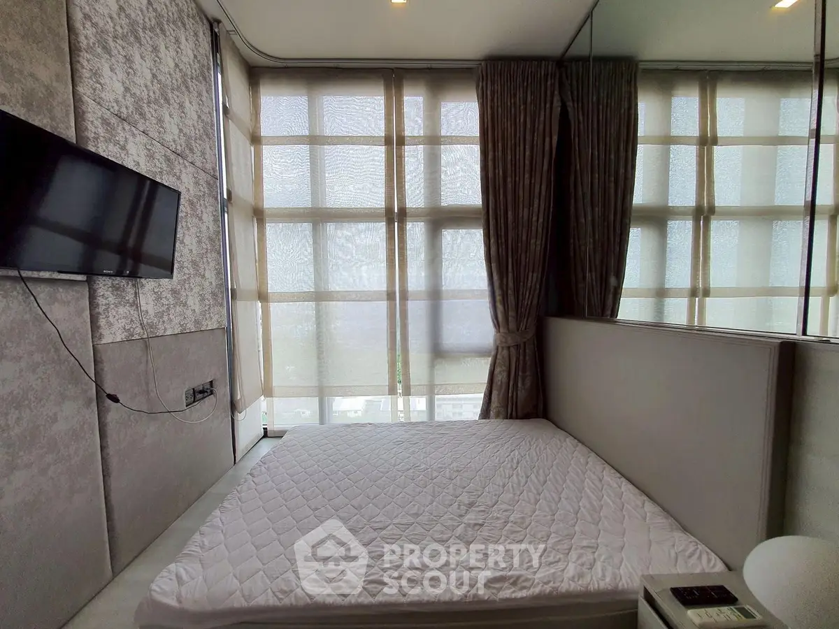 Modern bedroom with large windows and wall-mounted TV in a stylish apartment.