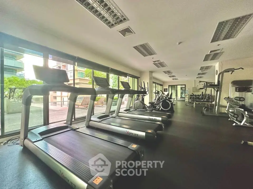 Spacious modern gym with state-of-the-art equipment and large windows offering natural light.