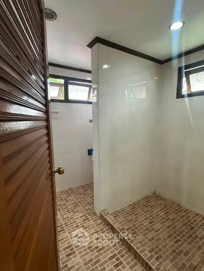 Spacious bathroom with tiled shower area and natural light from windows.
