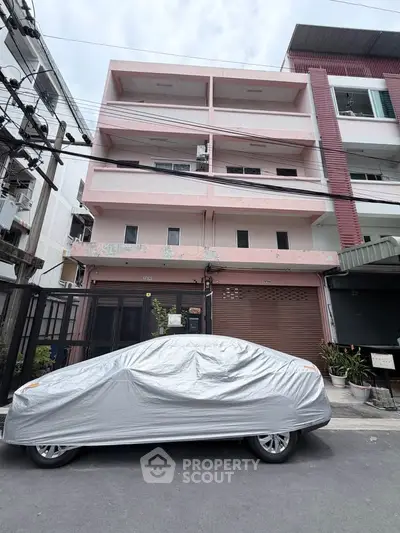 Charming three-story pink building with covered car in urban setting, ideal for residential or commercial use.