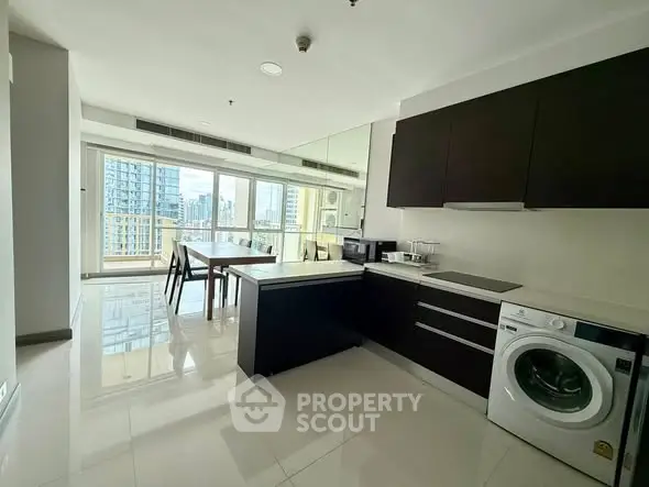 Modern kitchen with sleek cabinets and washing machine, featuring a dining area with city view.