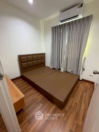 Cozy bedroom with wooden flooring and air conditioning, featuring a modern bed and stylish curtains.