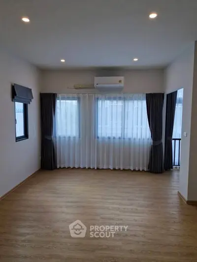 Spacious empty room with wooden flooring and large windows, perfect for customization.