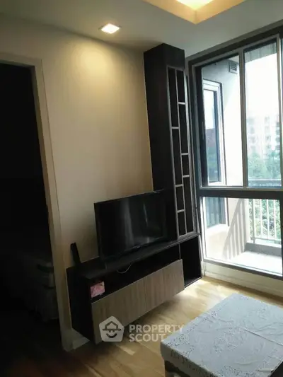 Modern living room with TV unit and large windows offering natural light and balcony access.