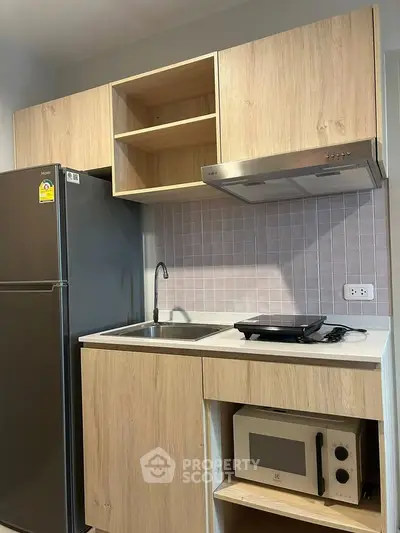 Modern compact kitchen with wooden cabinets, stainless steel fridge, and built-in microwave.