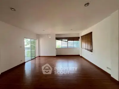Spacious empty living room with wooden flooring and large windows offering natural light.