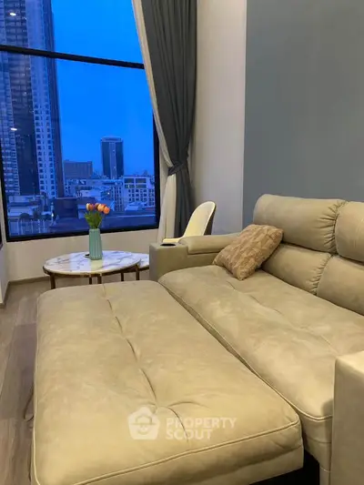 Modern living room with large window and city view, featuring a beige sofa and elegant decor.