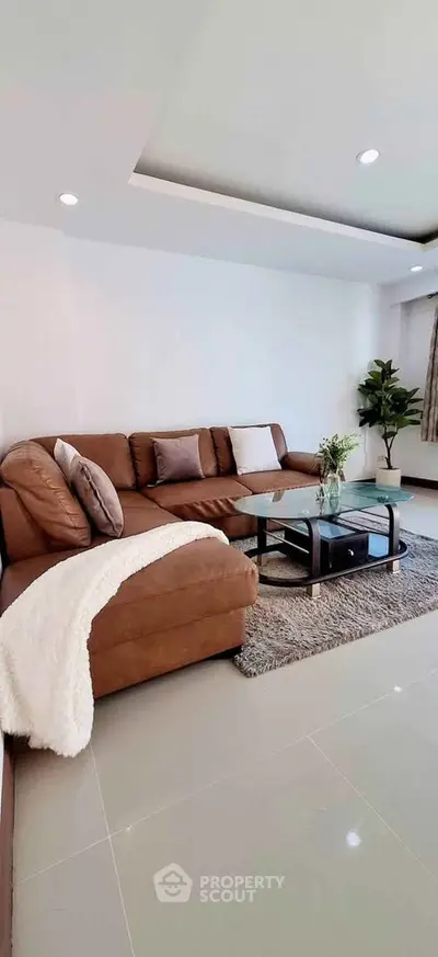 Modern living room with brown sectional sofa and glass coffee table, featuring elegant decor and natural light.