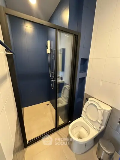 Modern bathroom with sleek shower and toilet in stylish blue and white design.