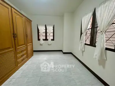 Spacious bedroom with large wooden wardrobe and tiled flooring, featuring natural light from multiple windows.