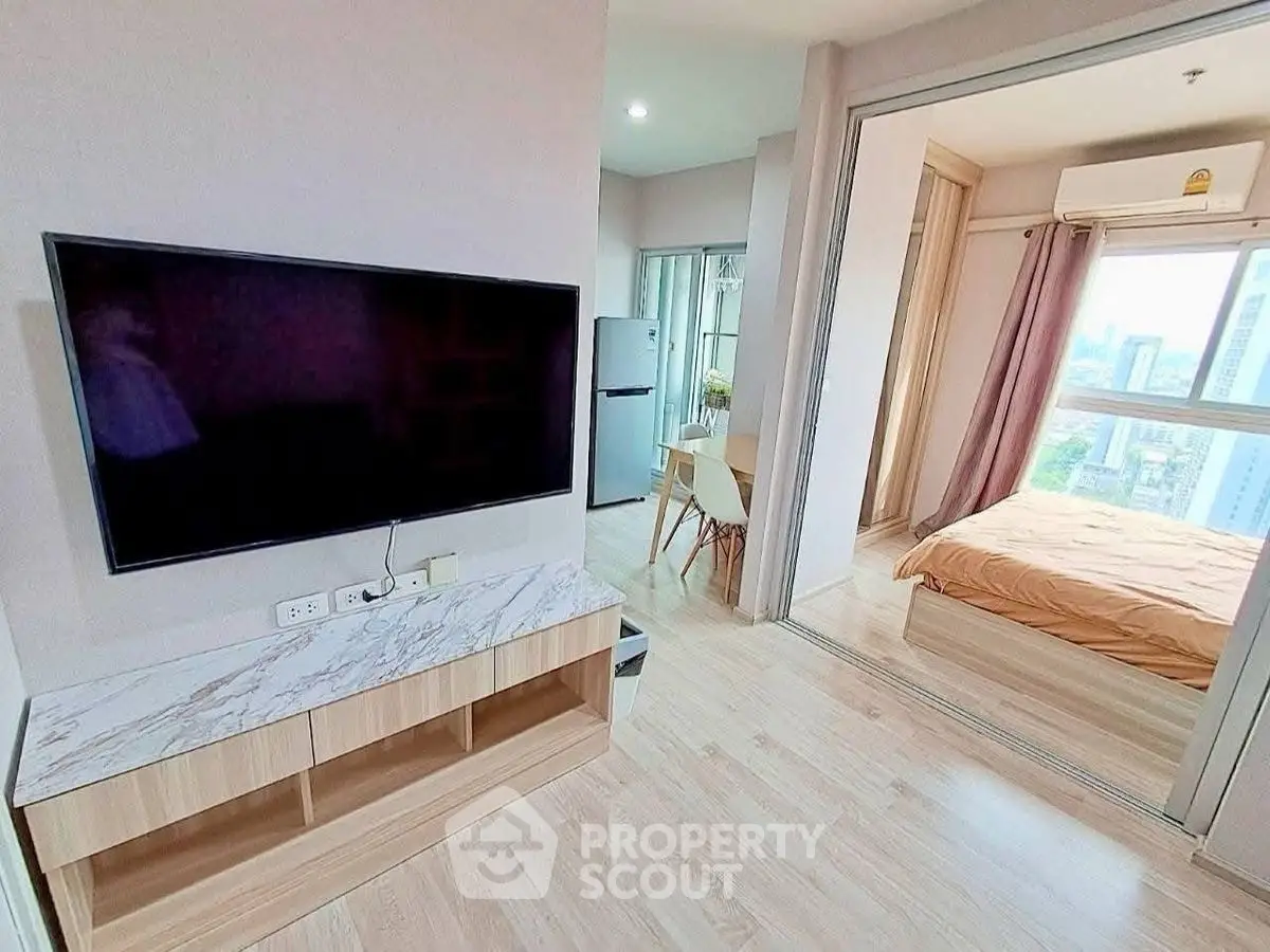 Modern apartment with open living room and bedroom, featuring sleek TV setup and city view.