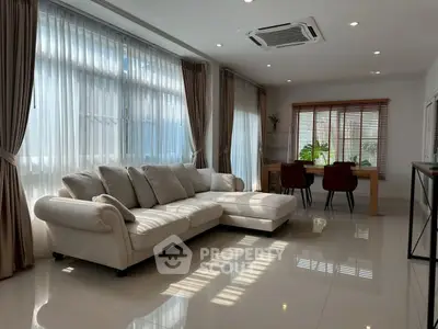 Spacious modern living room with elegant sofa and dining area, featuring large windows and natural light.