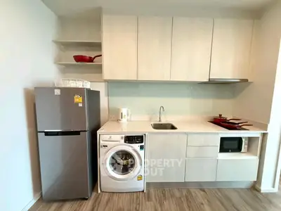 Modern kitchen with sleek cabinetry, washing machine, fridge, and microwave in a compact layout.