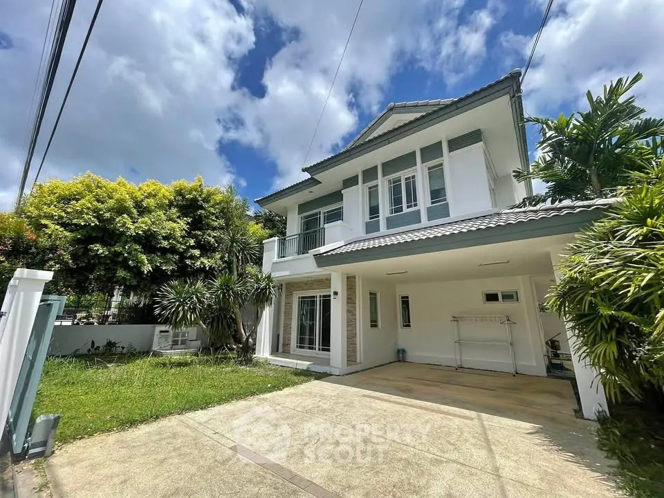 Charming two-story house with lush garden and spacious driveway under a clear blue sky.