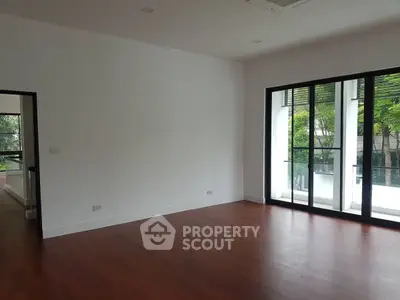 Spacious empty room with hardwood floors and large windows overlooking greenery.