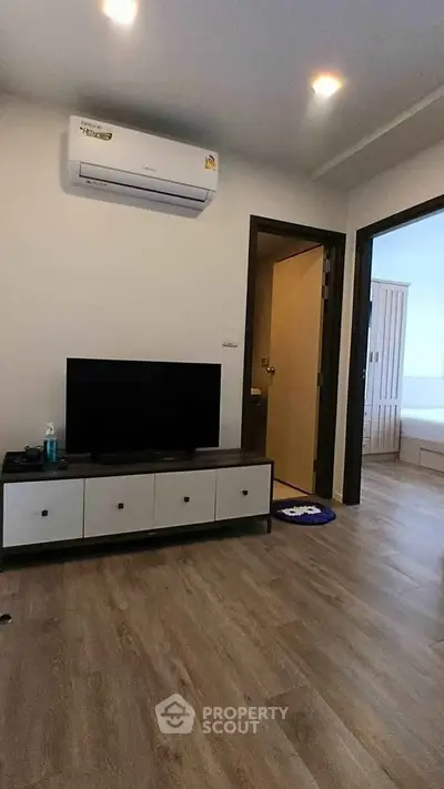 Modern living room with sleek TV stand and air conditioning, featuring wooden flooring and open doorway to bedroom.