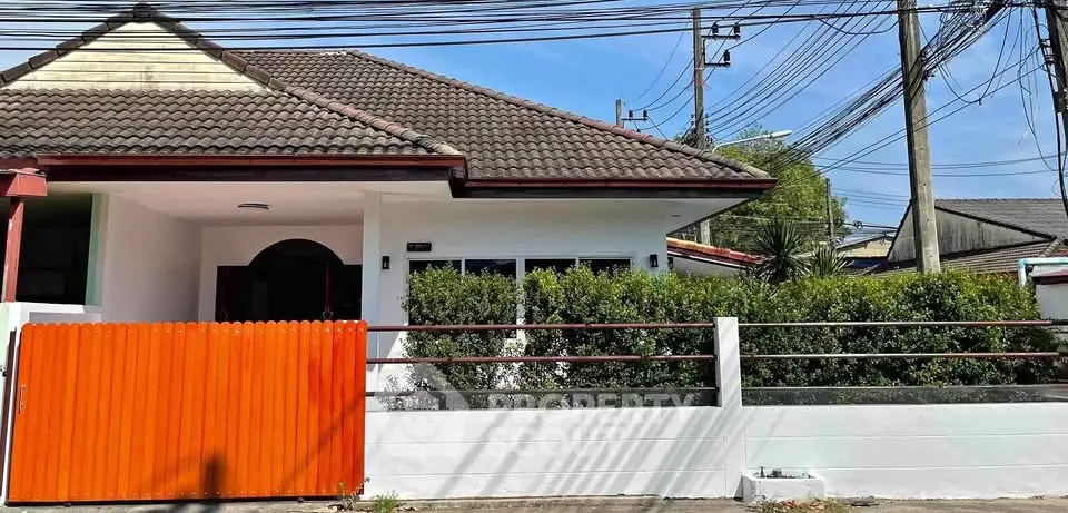 Charming single-story house with red gate and lush greenery, perfect for family living.
