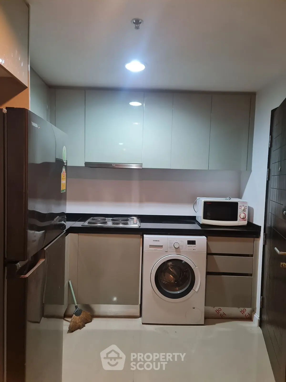 Modern kitchen with sleek appliances including fridge, washing machine, and microwave in compact layout.