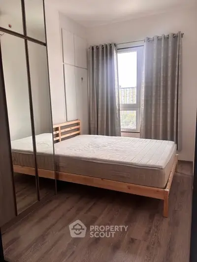 Cozy bedroom with wooden flooring and large window offering natural light.