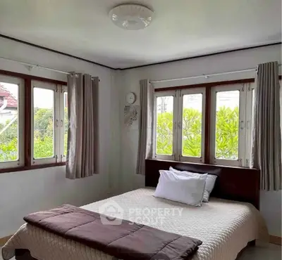 Charming bedroom with large windows and garden view, perfect for serene living.