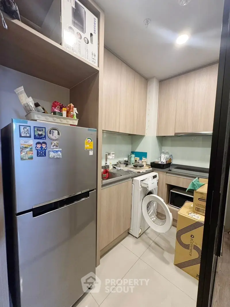 Modern kitchen with sleek cabinets, fridge, and washing machine in compact layout.