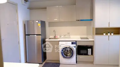 Modern kitchen with sleek cabinets, fridge, washing machine, and microwave in a compact layout.