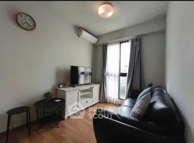 Cozy living room with modern decor, featuring a sleek black sofa, flat-screen TV, and natural light from large window.