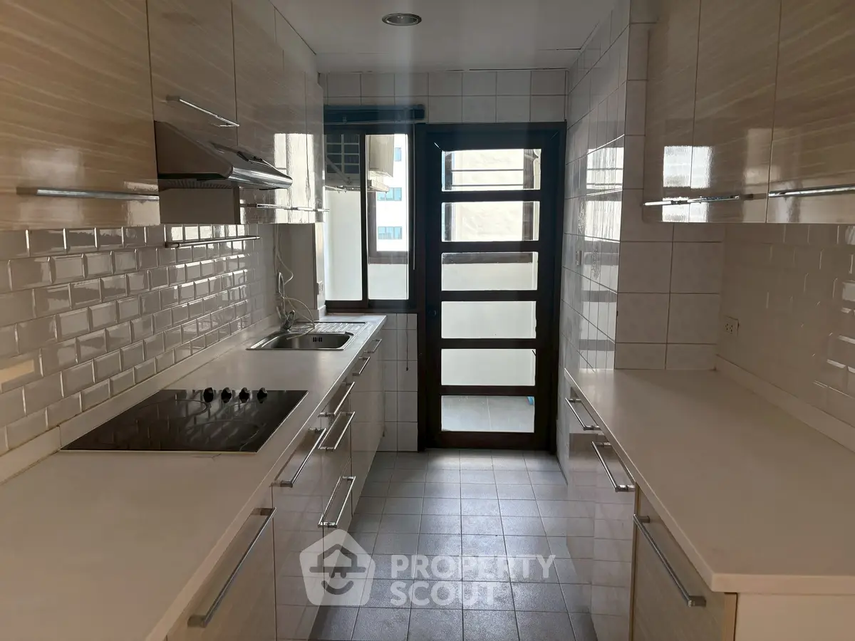 Modern kitchen with sleek cabinetry and electric cooktop in a bright, narrow layout.