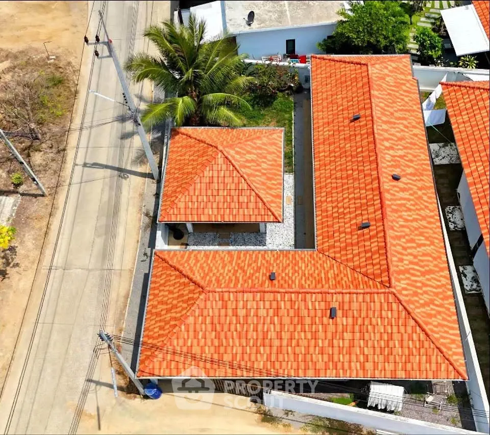 Aerial view of a property with vibrant red-tiled roofs and lush greenery, showcasing a spacious layout.