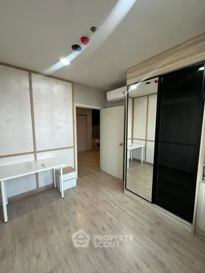 Spacious bedroom with modern design and ample natural light, featuring sleek mirrored wardrobe and wooden flooring.