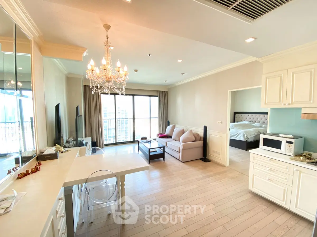 Spacious open-plan living room with elegant chandelier and modern kitchen in luxury apartment.