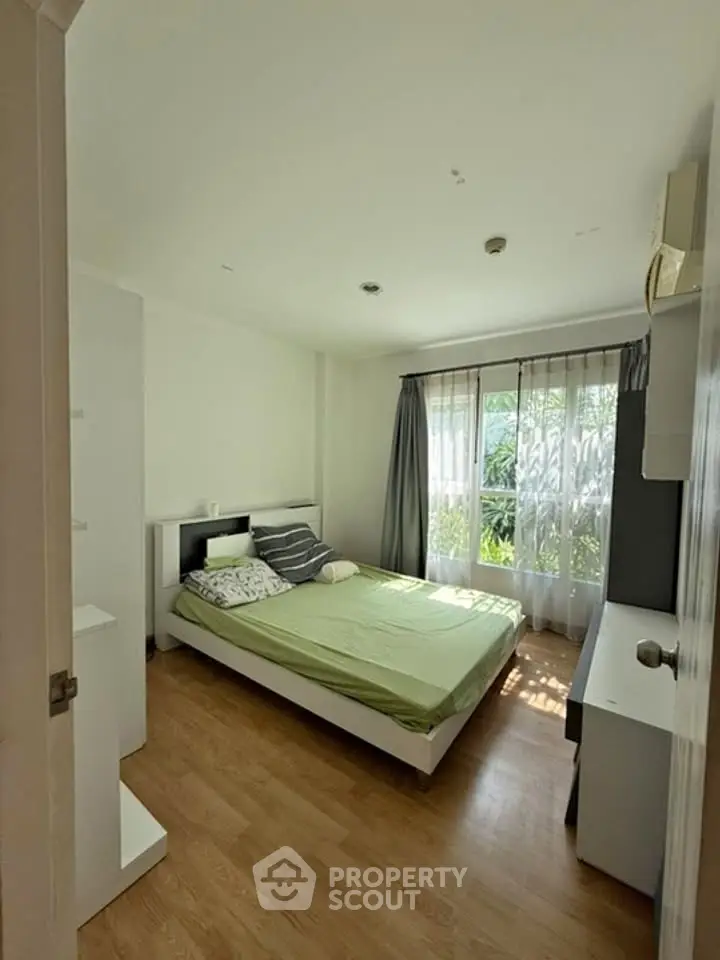 Bright and cozy bedroom with large window and wooden flooring, perfect for relaxation.