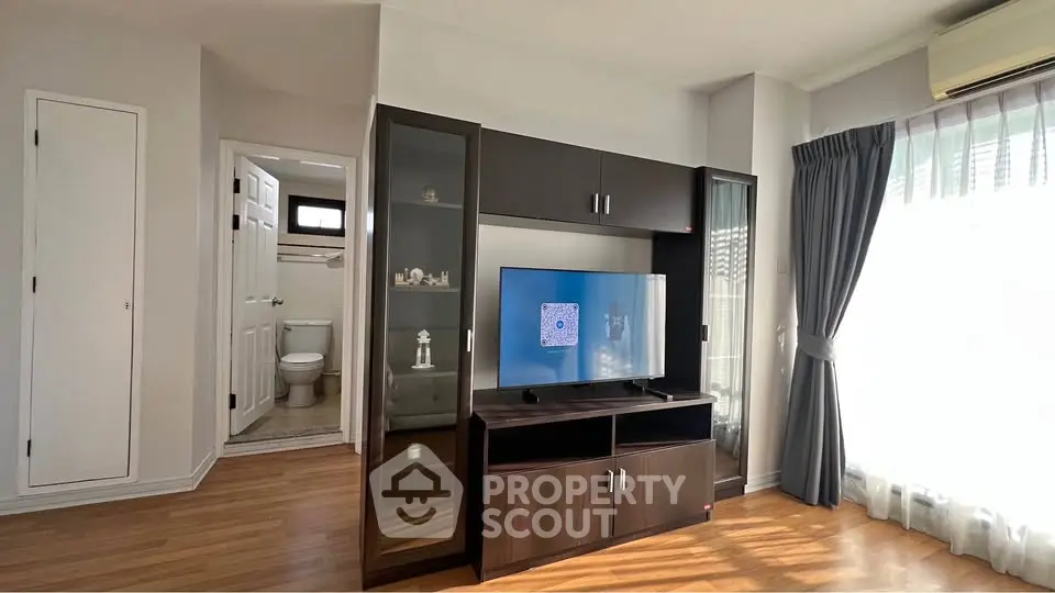 Modern living room with TV unit and natural light, adjacent to a bathroom.