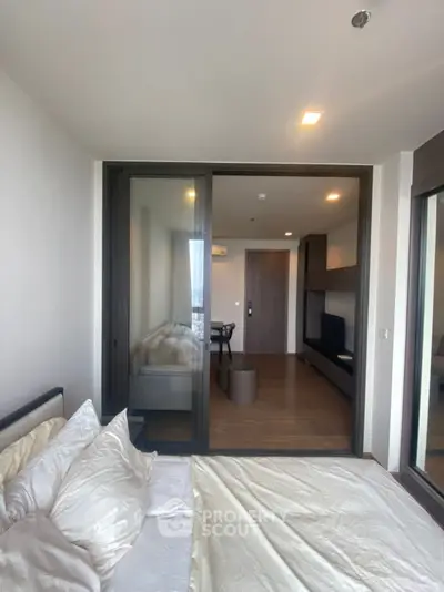 Modern bedroom with glass partition and cozy living area, sleek design and natural light.