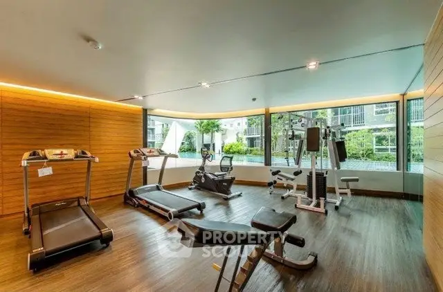 Modern gym with large windows and fitness equipment in luxury apartment complex.