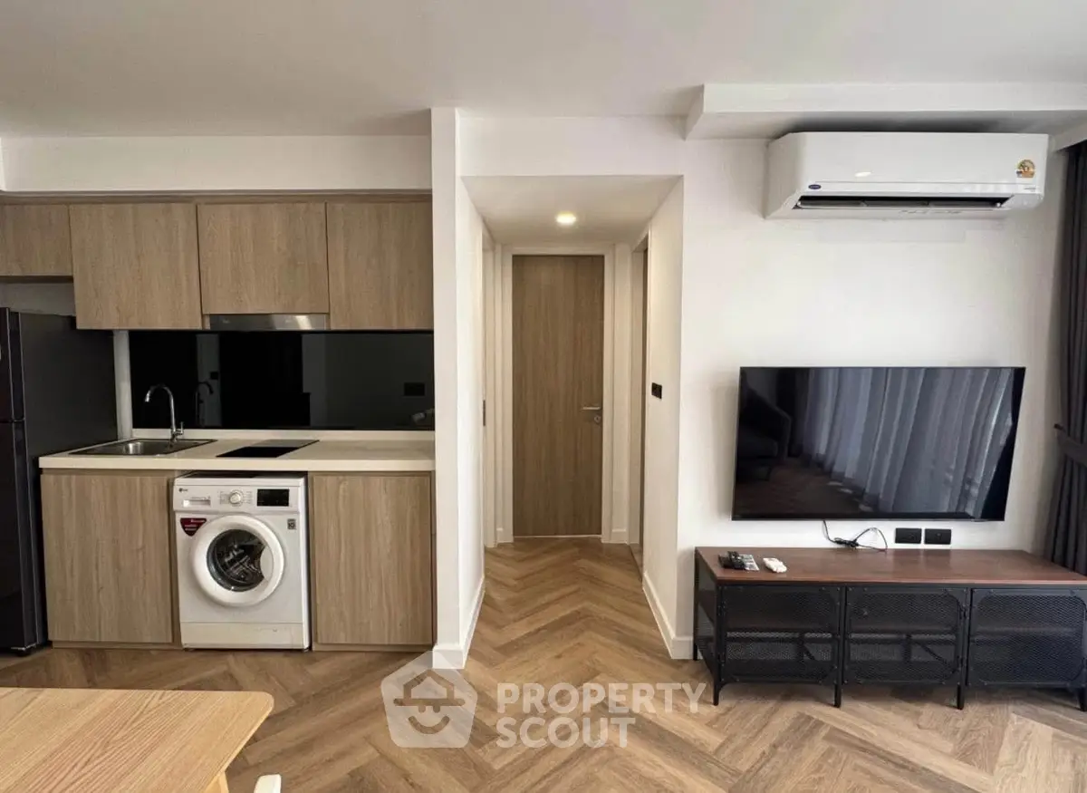 Modern apartment interior with kitchen and living area featuring wooden flooring and built-in appliances.