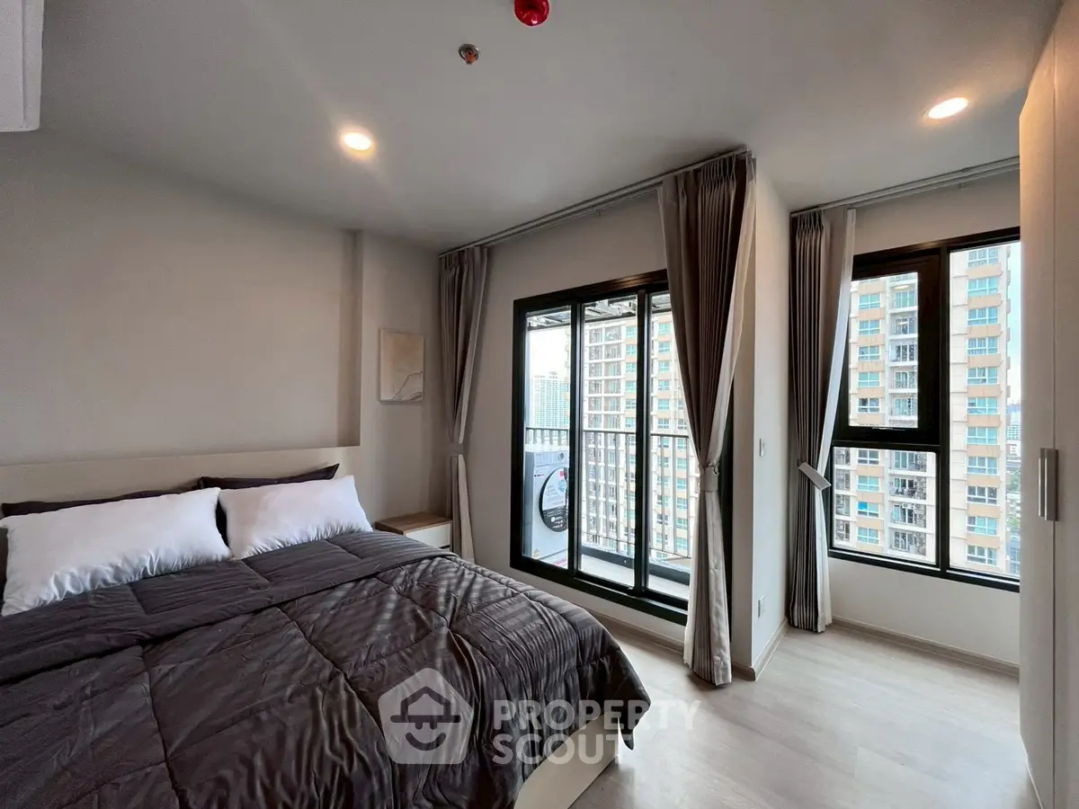 Modern bedroom with large windows and city view, featuring a cozy bed and elegant curtains.