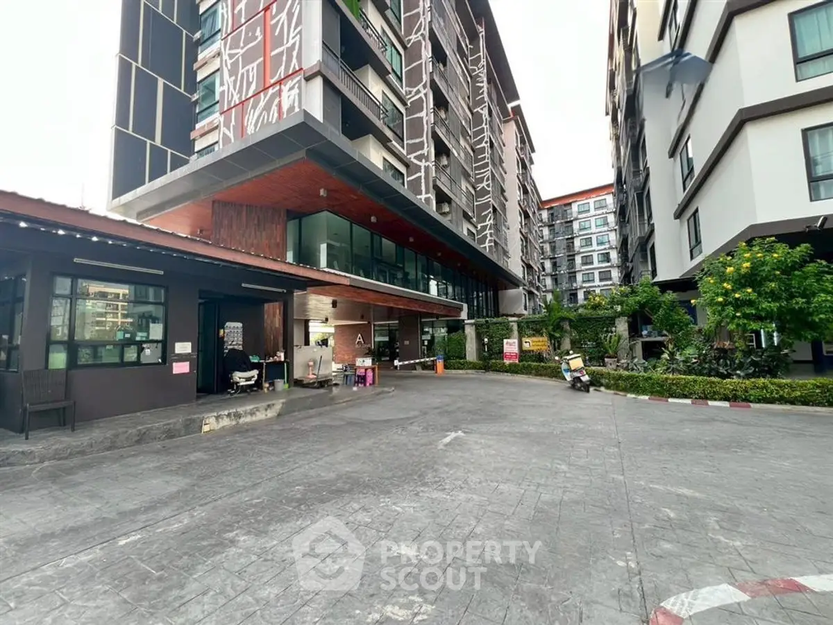 Modern apartment building exterior with landscaped entrance and parking area.