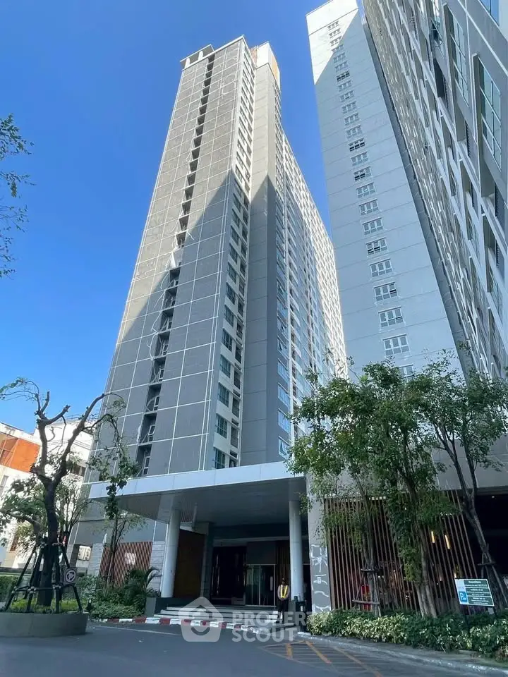 Modern high-rise building with sleek design and lush greenery at entrance.