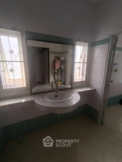 Spacious bathroom with large mirror and natural light from two windows.