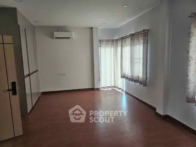 Spacious empty room with wooden flooring and large windows, perfect for customization.