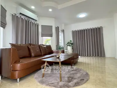 Spacious living room with modern brown leather sofa and elegant curtains, perfect for relaxation.