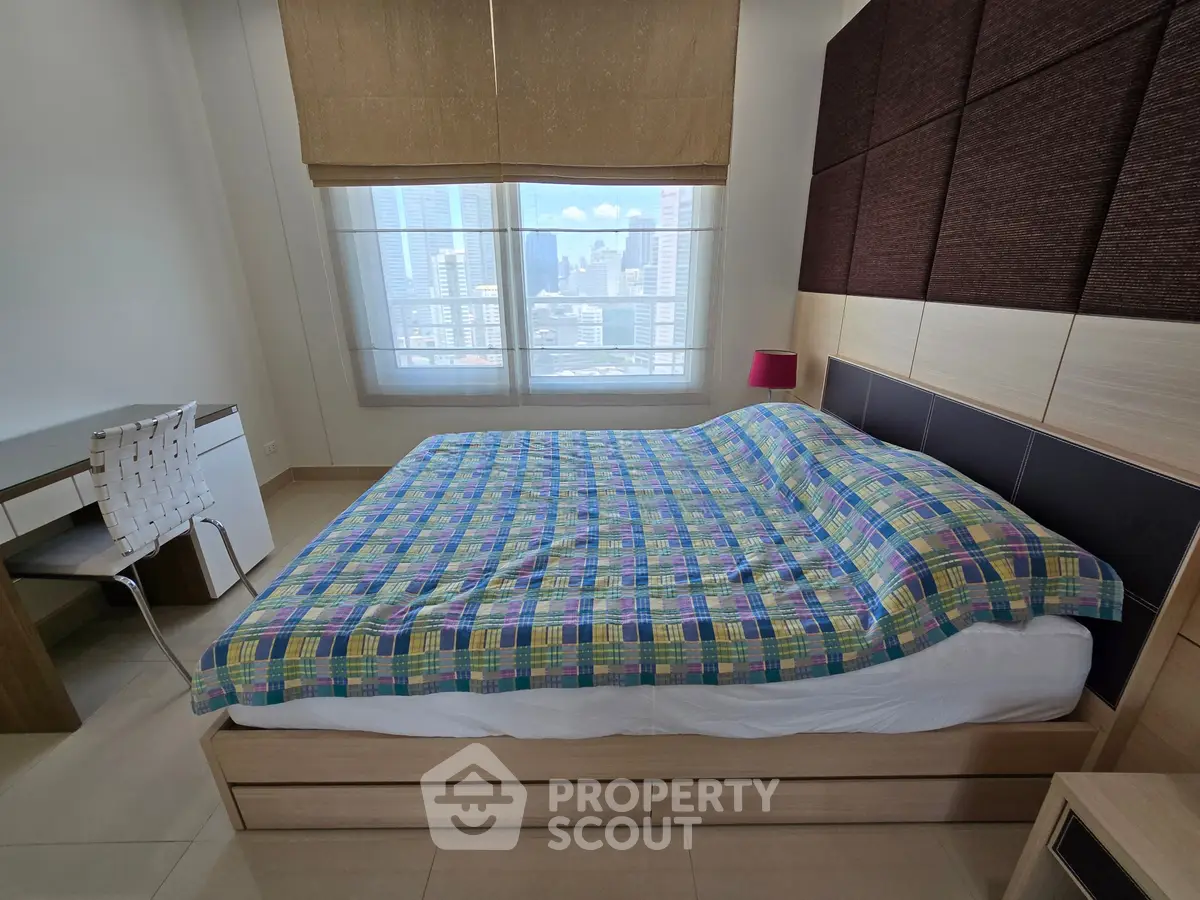 Modern bedroom with city view, featuring a stylish bed and work desk, perfect for urban living.