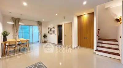 Spacious modern living area with dining set and staircase, featuring elegant decor and ample natural light.