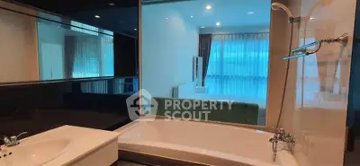 Modern bathroom with bathtub and view into a stylish bedroom through glass partition.